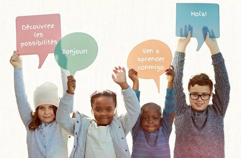 Kids hold up signs in the shape of speech bubbles that contain French and Spanish words and phrases.