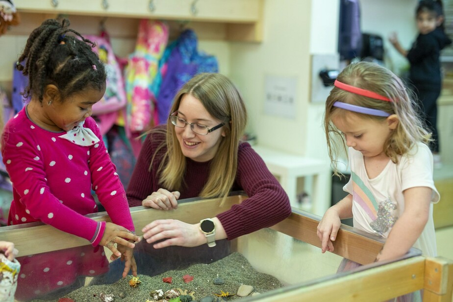 teacher playing with young students at sand table