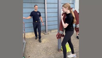 A student carries a folded fire hose over her shoulder while a firemedic looks on.