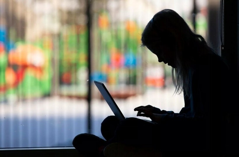 a student is silhouetted sitting on the floor with a laptop.