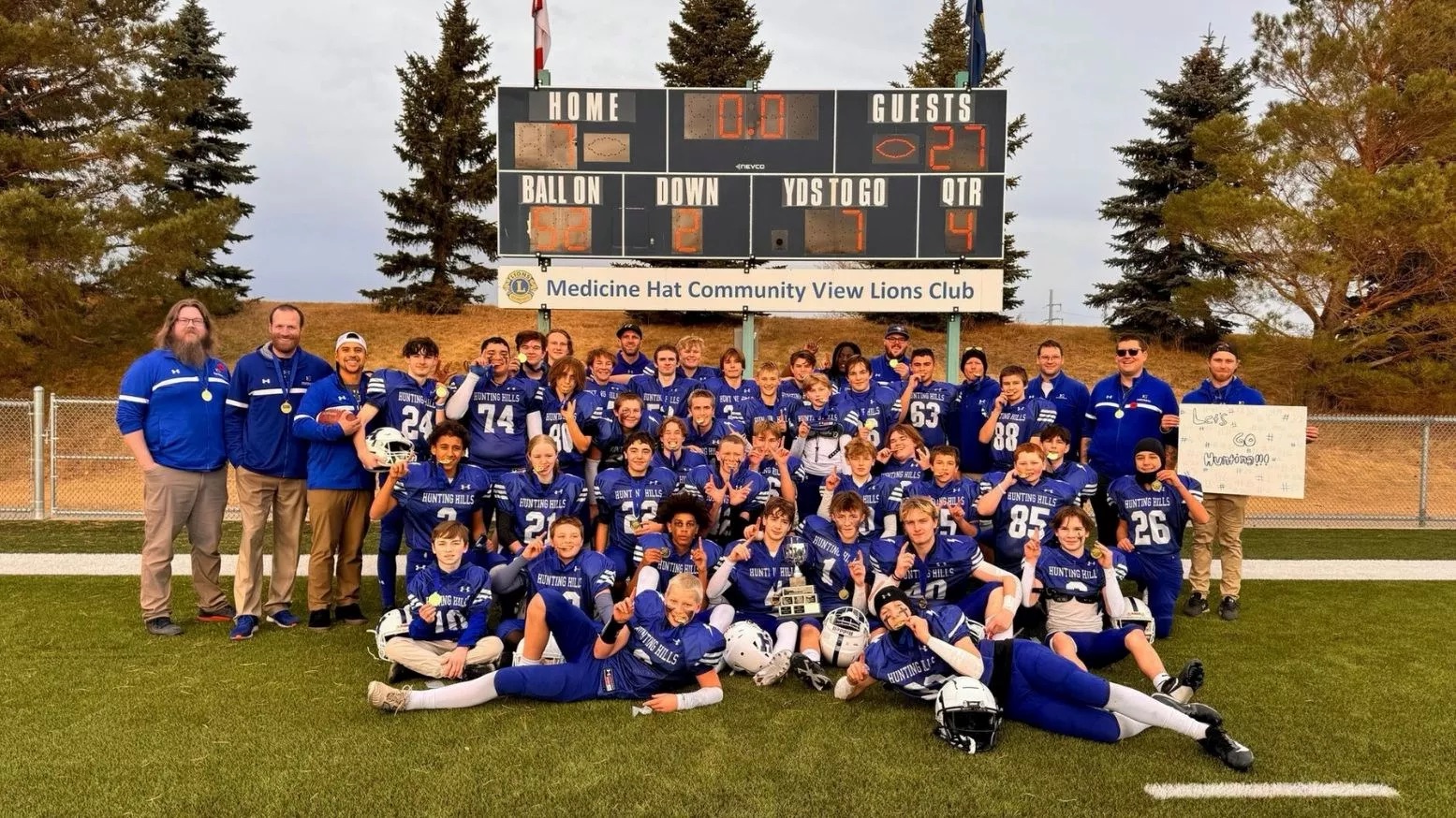 the football team poses on the field in front of the score board.